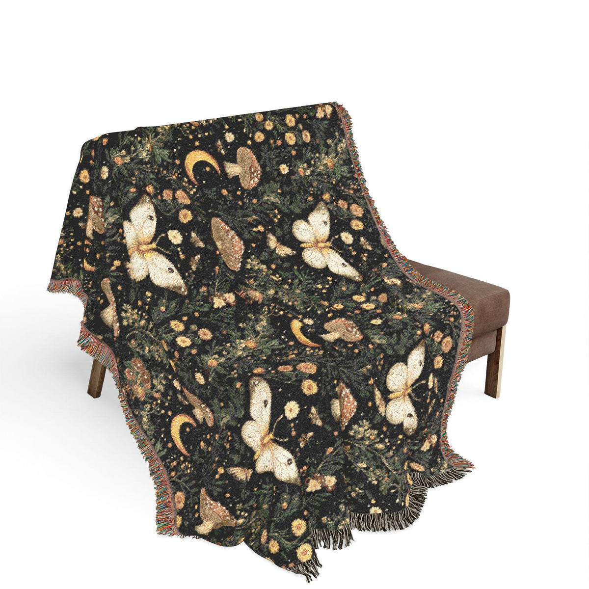 A dark patterned throw blanket with fringed edges draped over a brown upholstered chair against a plain white background. The blanket features a detailed print of butterflies, mushrooms, pinecones, and crescent moons in cream, gold, and light brown tones.
