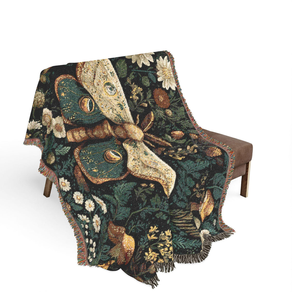 A woven throw blanket with a large moth motif and floral pattern, draped over a brown upholstered bench against a plain white background.