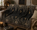 Black woven cotton throw blanket with celestial moon phases and daisy floral border, draped over a boho-style sofa