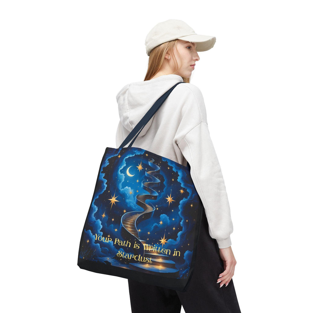 Woman wearing Cosmic Stardust Tote Bag — deep blue celestial design with gold stars, crescent moon, and "Your Path is Written in Stardust" script, navy handle