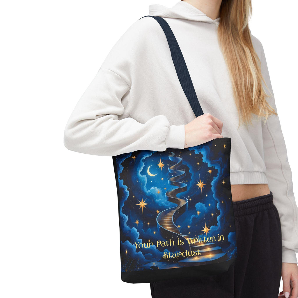 Woman wearing Cosmic Stardust Tote Bag on shoulder — celestial deep blue design with gold stars, crescent moon, swirling stardust path, and script quote, navy handle, side view