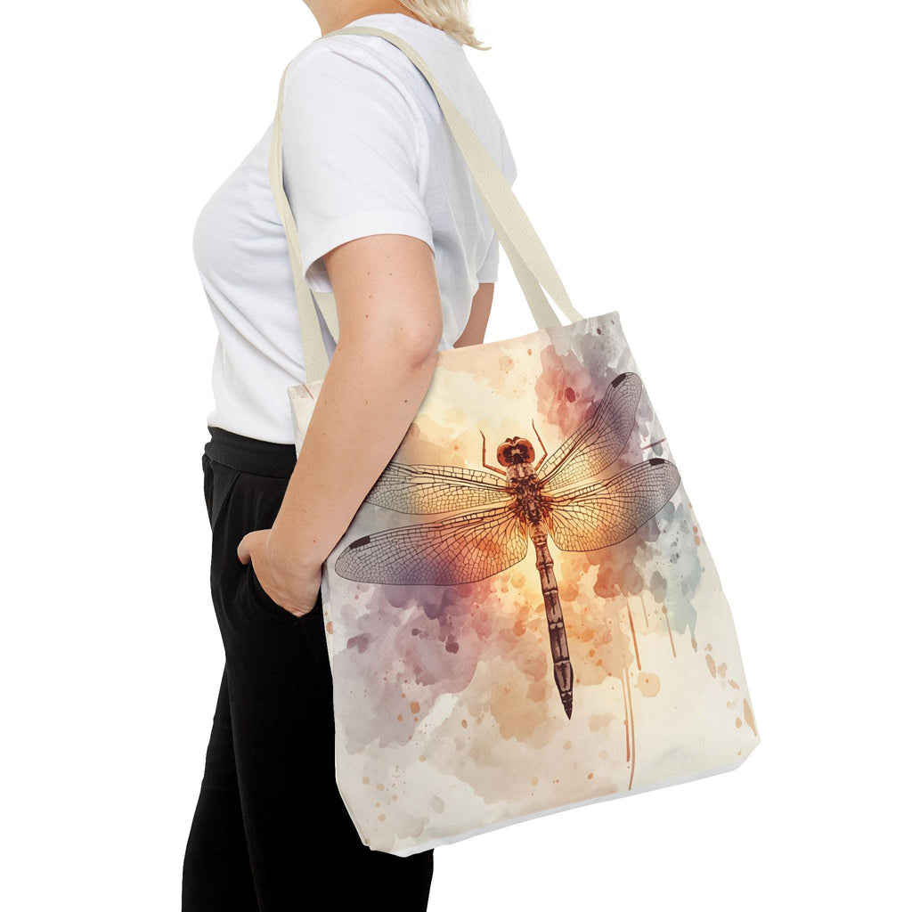 Woman wearing Watercolor Dragonfly Tote Bag — vintage dragonfly illustration on soft watercolor wash background in cream, blush, and sage tones, natural canvas handle, side view
