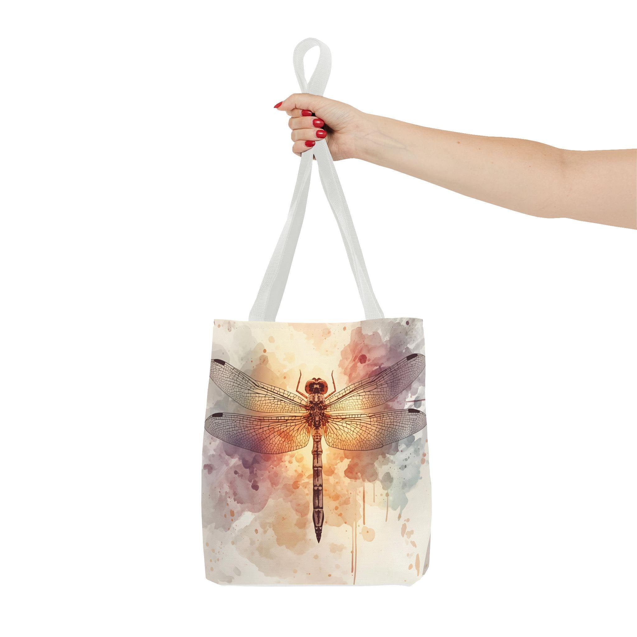 Watercolor Dragonfly Tote Bag held by handle — vintage dragonfly illustration on soft watercolor wash background in cream, blush, and sage tones, natural canvas handle
