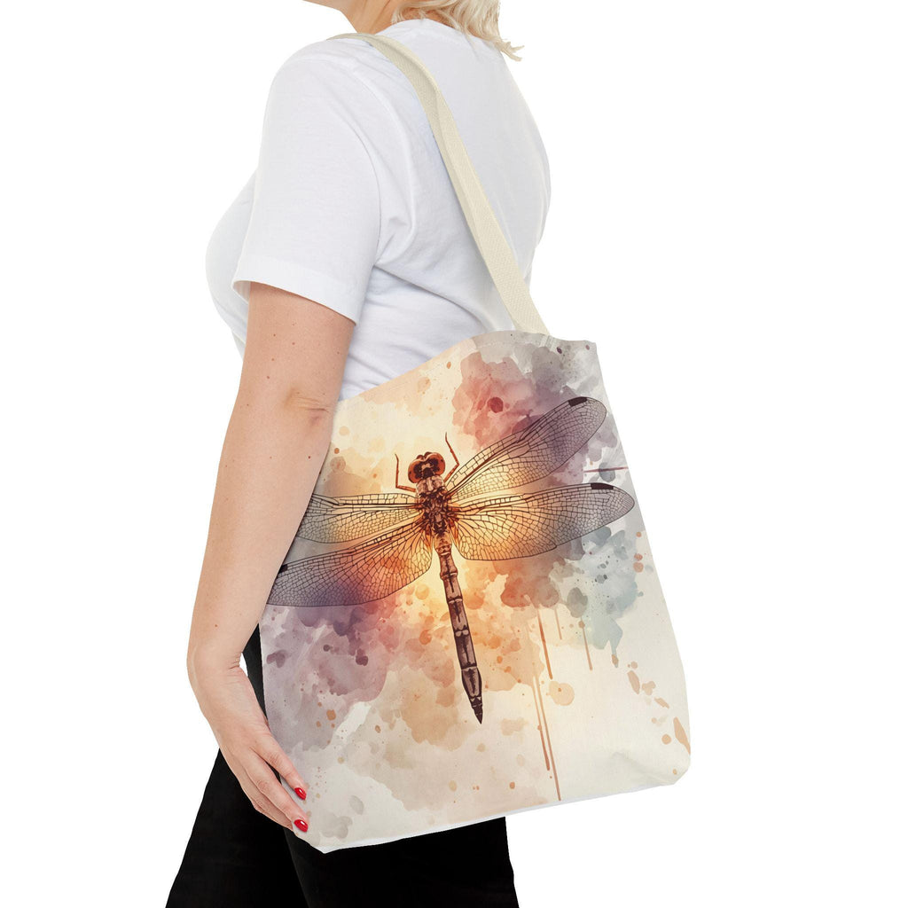 Woman wearing Watercolor Dragonfly Tote Bag — vintage dragonfly illustration on soft watercolor wash background in cream, blush, and sage tones, natural canvas handle, side view