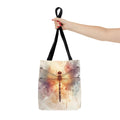 Watercolor Dragonfly Tote Bag held by handle — vintage dragonfly illustration on soft watercolor wash background in cream, blush, and sage tones, black handle
