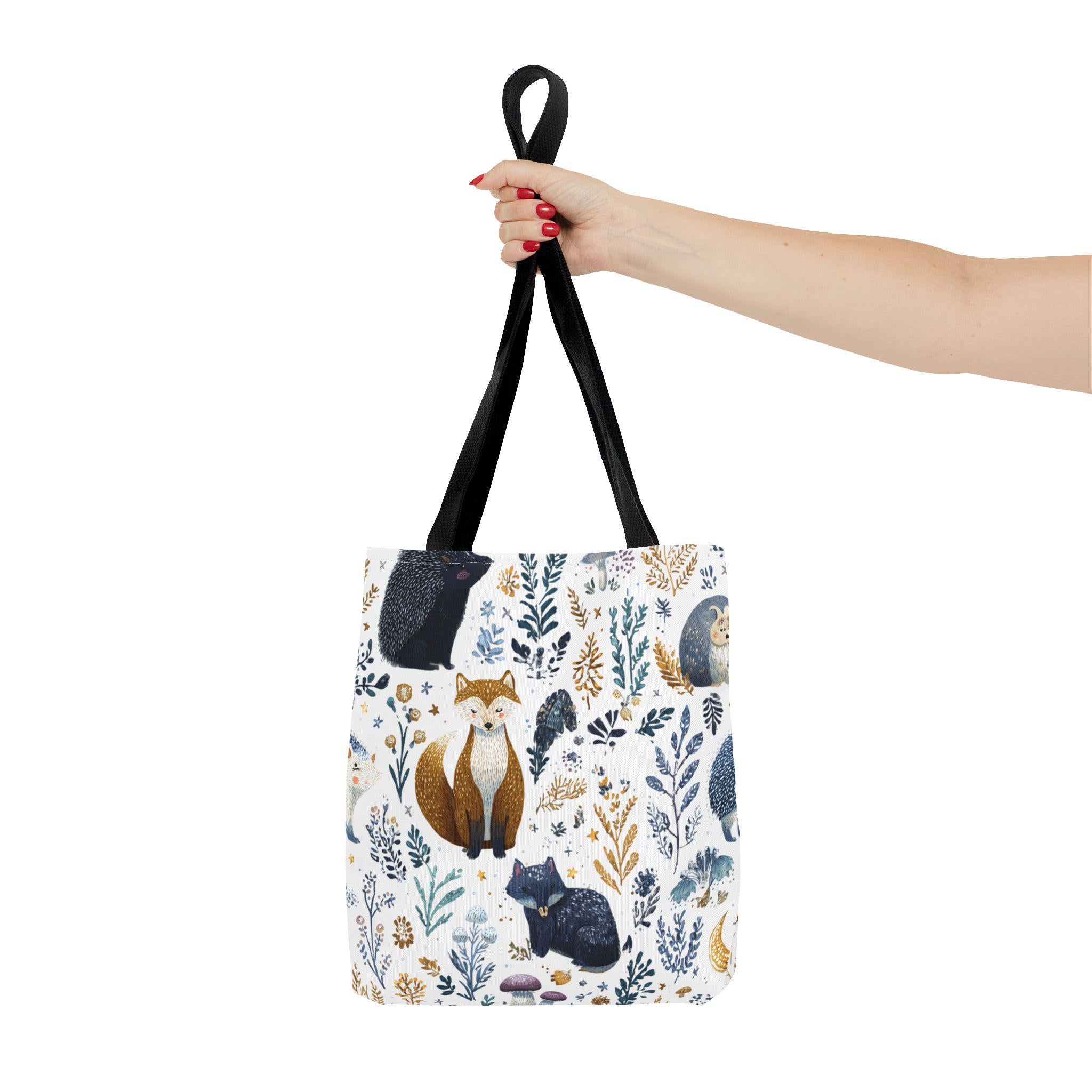 Woodland Fox and Hedgehog Tote Bag held by handle — forest animal print with foxes, hedgehogs, and floral sprigs in navy, amber, and gray, black handle