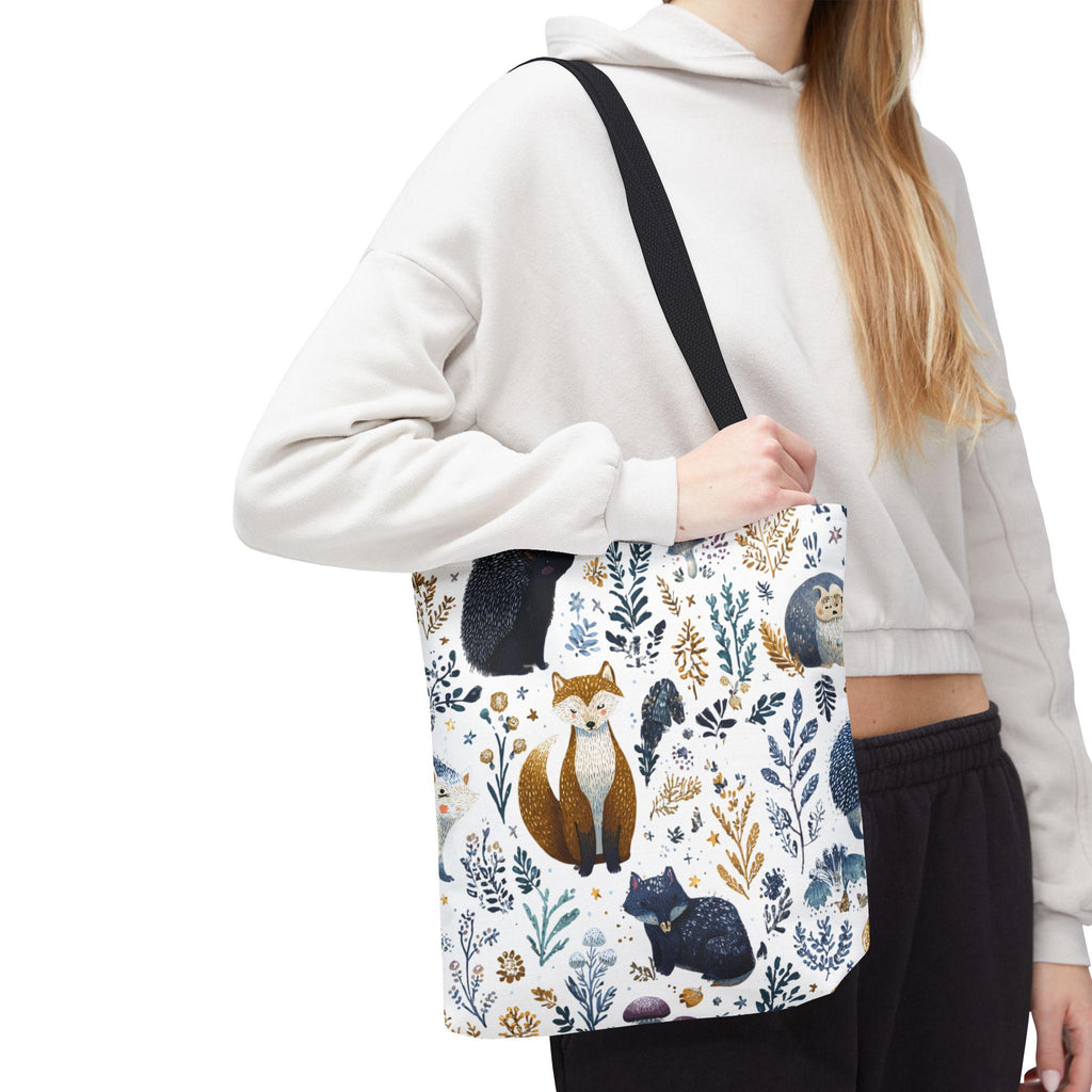 Woman wearing Woodland Fox and Hedgehog Tote Bag — forest animal print with foxes, hedgehogs, and floral sprigs in navy, amber, and gray, black handle, cropped hoodie styling