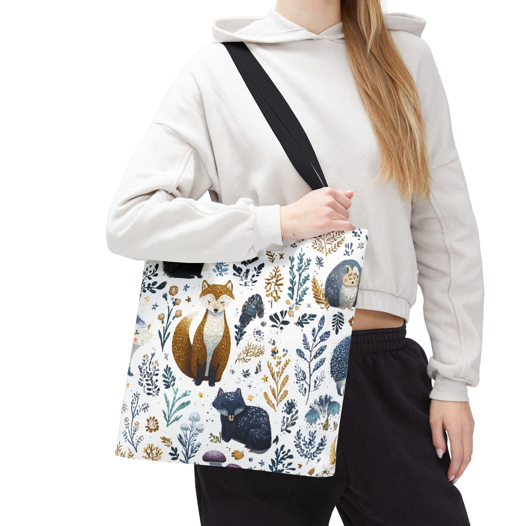 Woman wearing Woodland Fox and Hedgehog Tote Bag on shoulder — forest animal print with foxes, hedgehogs, and floral sprigs in navy, amber, and gray, black handle, cropped hoodie styling
