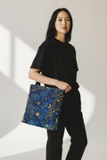 Woman carrying Celestial Navy Blue Tote Bag with gold moon and stars pattern — boho night sky canvas tote
