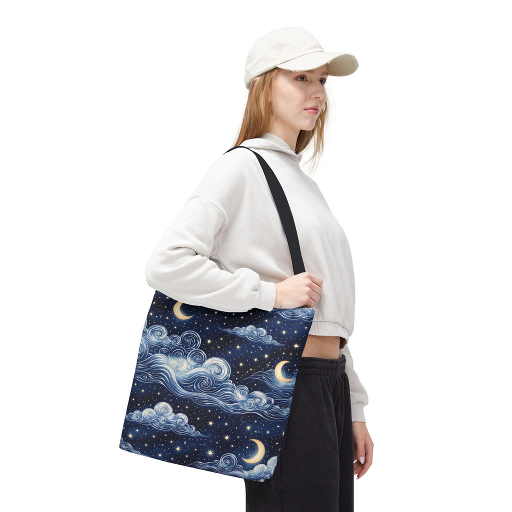 Moon and whimsical clouds tote bag worn cross body — woman in casual outfit with cap carrying navy night sky cloud print tote
